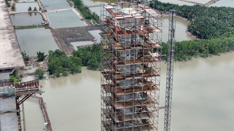 Aerial shot of construction scaffolding by a river, surrounded by lush greenery.