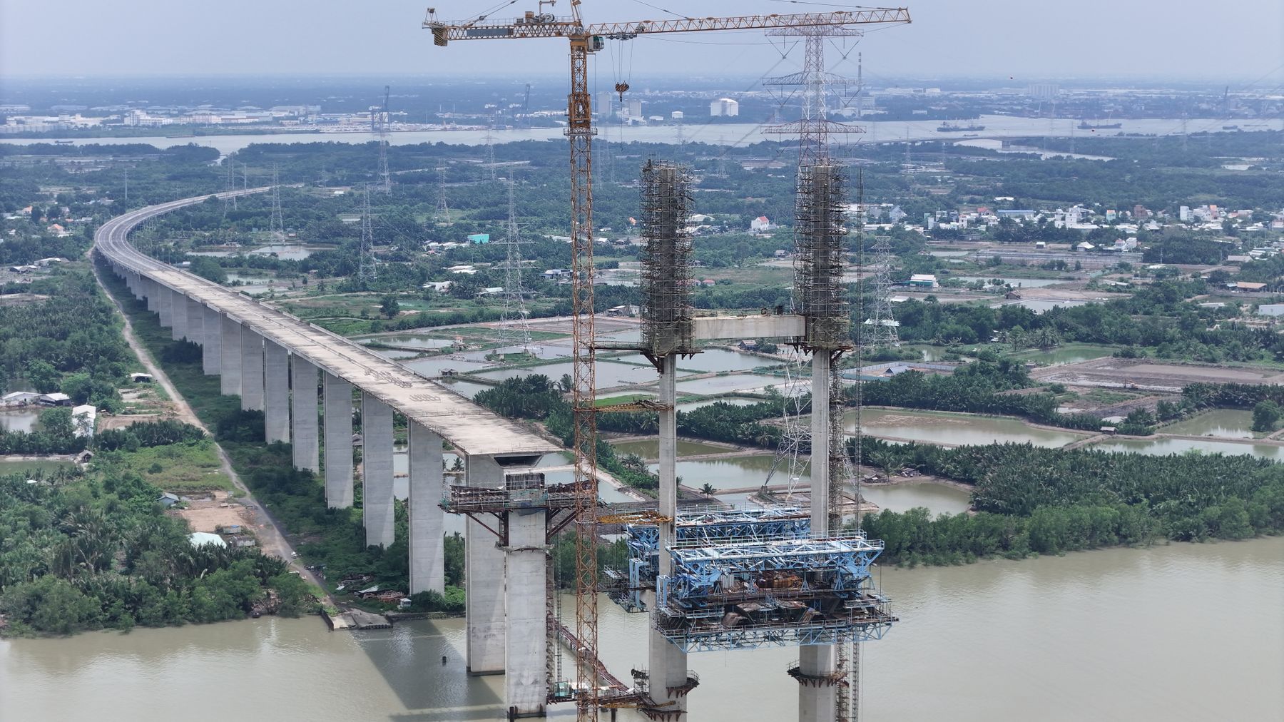 Aerial view of a bridge construction over a river in Vietnam, showcasing cranes and scaffolding.