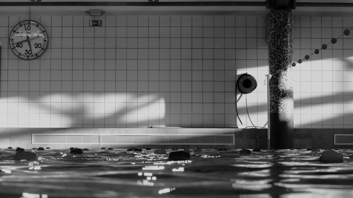 Monochrome view of an indoor swimming pool with a pace clock and tiled lane markers