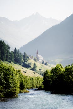 A picturesque Alpine church nestled among lush hills and majestic mountains.