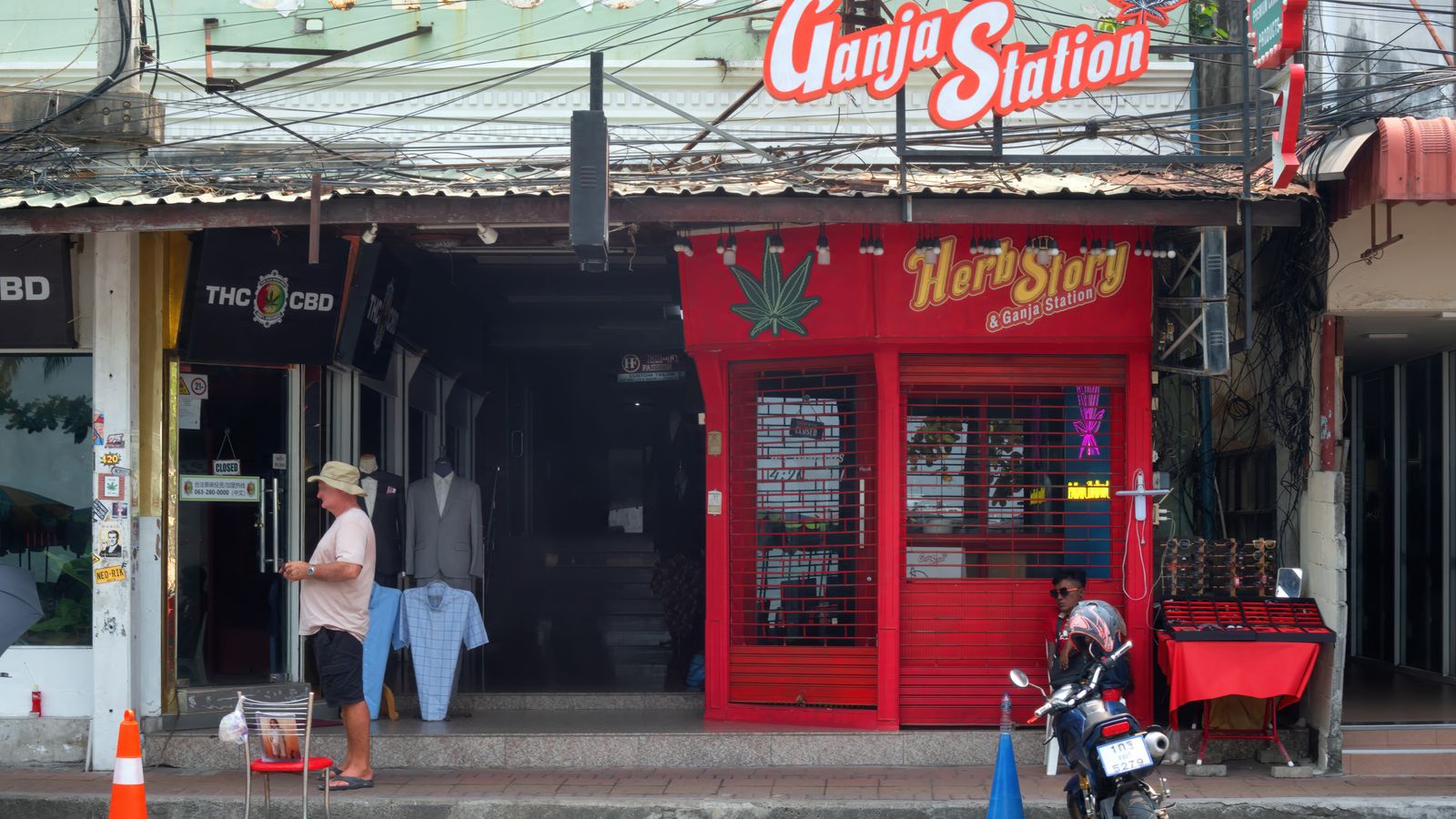 Front view of a Ganja Station store in Pattaya, showcasing cannabis-themed signage and street vendors.