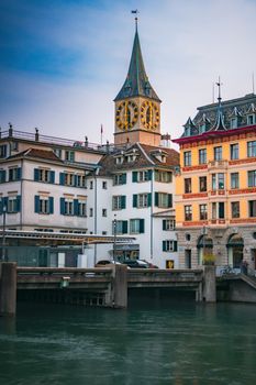 Charming evening view of St. Peter's Church by the river in Zürich, Switzerland, featuring iconic architecture.