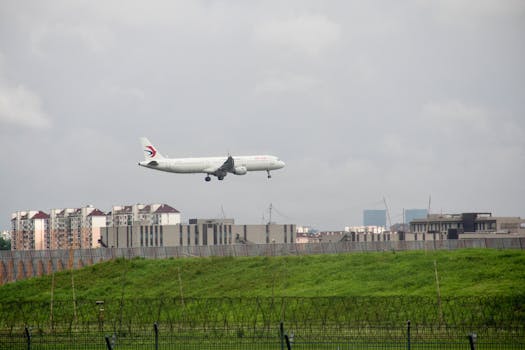 A commercial airplane landing near city buildings on a cloudy day, showcasing urban life.