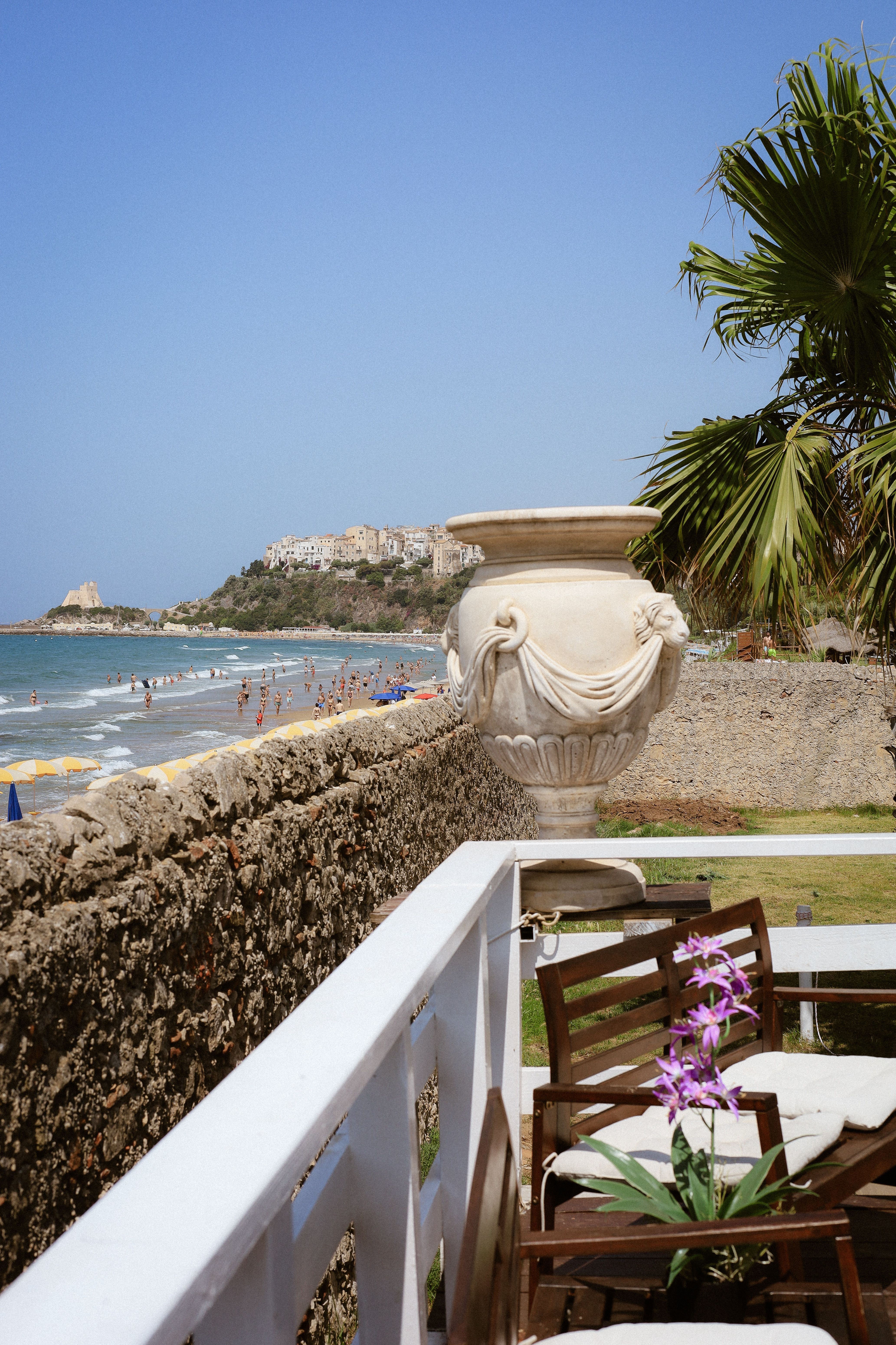 Scenic view of a Mediterranean beach and historic town from a sunlit patio.