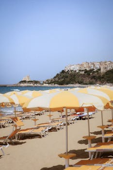 Picturesque beach scene with yellow umbrellas and a coastal village in the background.