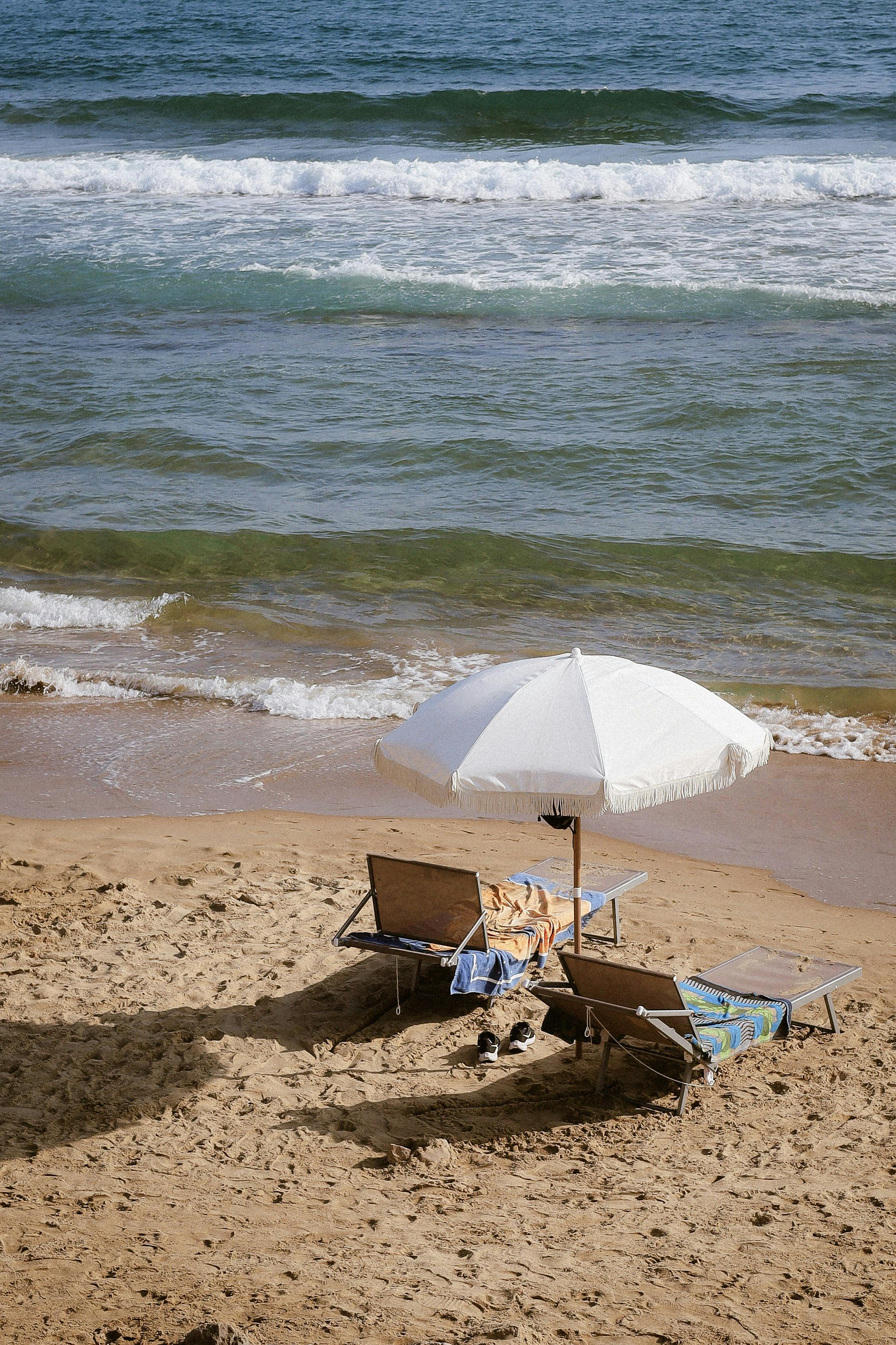 A serene beach setup featuring chairs and a sunshade by the ocean, ideal for relaxation.