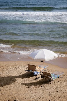 A serene beach setup featuring chairs and a sunshade by the ocean, ideal for relaxation.