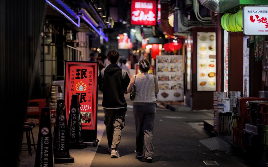A couple strolls through a lively street in Kobe, Japan, surrounded by glowing signs and vibrant nightlife.
