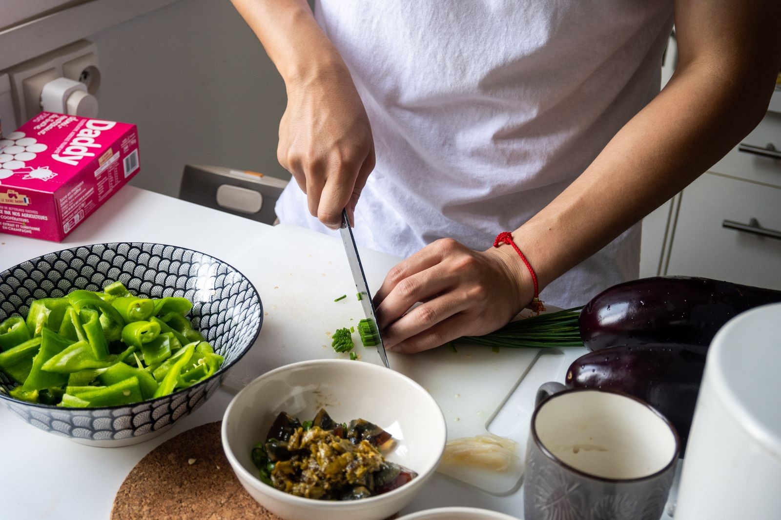 Close-up of a person slicing green onions and preparing vegetables in a kitchen setting.