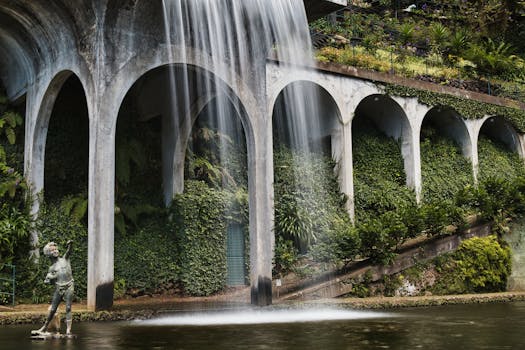 Elegant stone arches and a classical statue in a lush, green garden waterfall scene.
