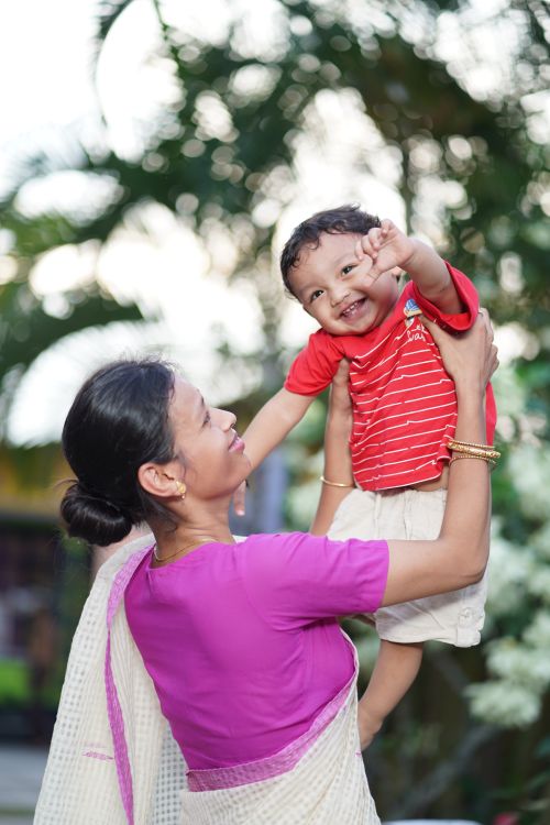 Free A mother joyfully lifts her smiling child in a vibrant outdoor setting, capturing a moment of happiness and bonding. Stock Photo