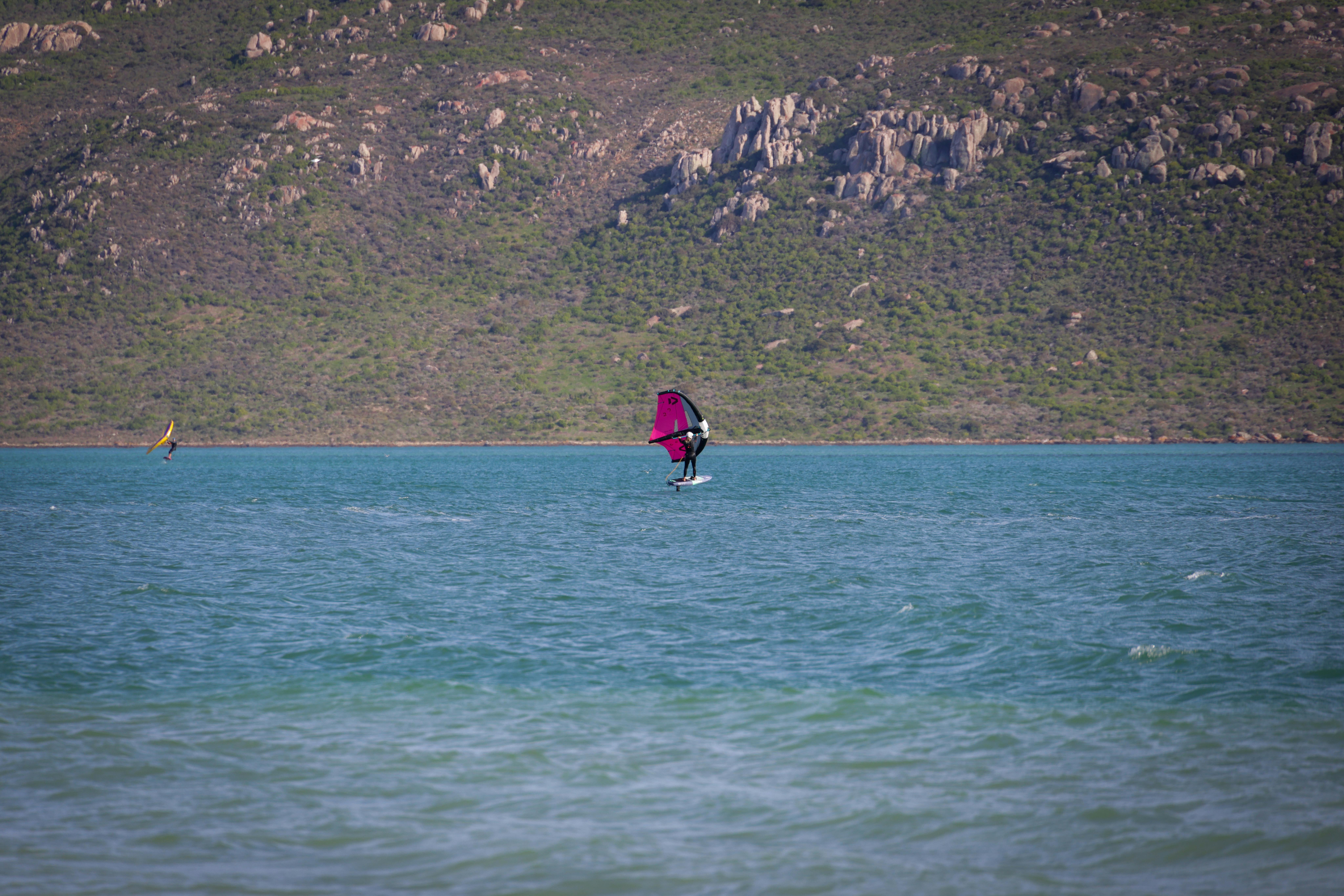 Windsurfers enjoying an adventure on pristine turquoise waters with scenic rocky hills in the background.