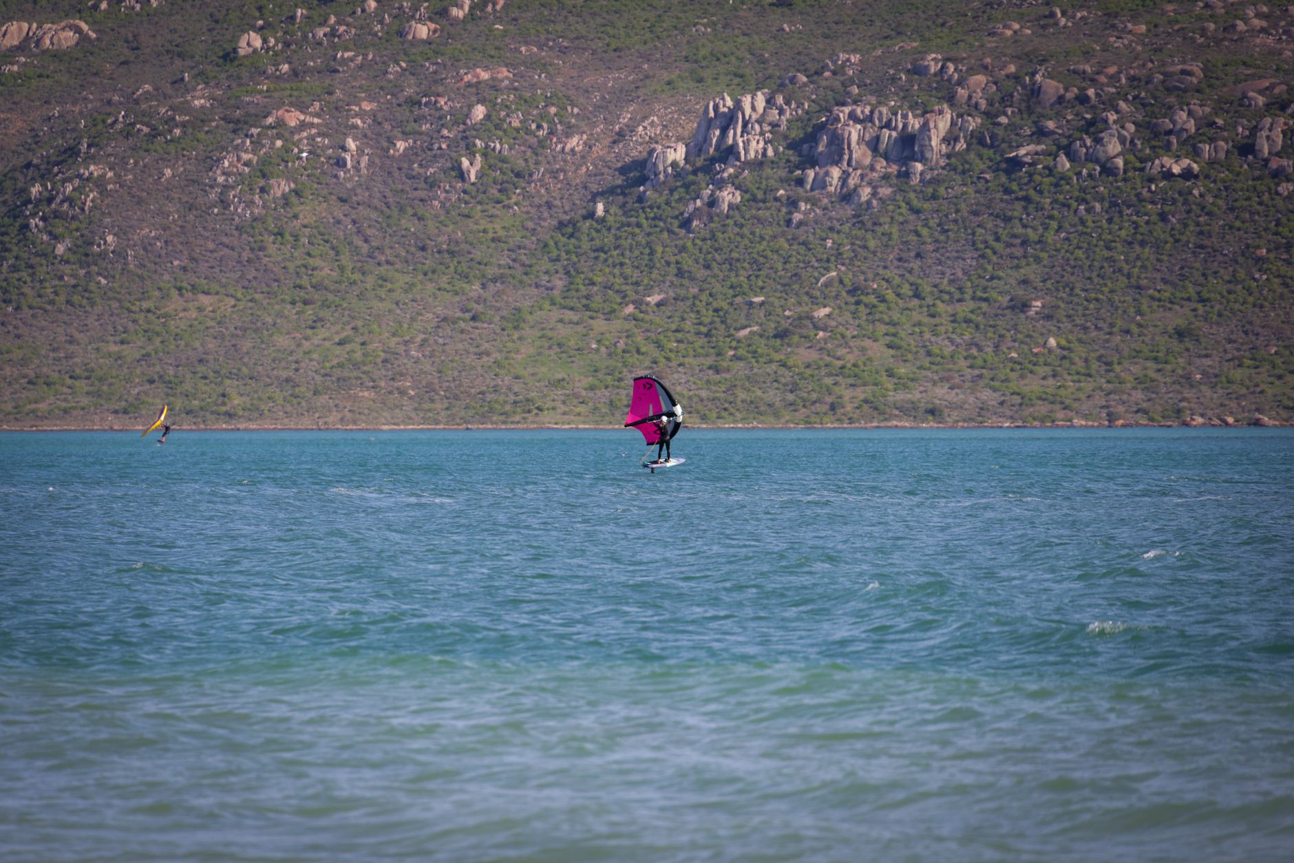 Windsurfers enjoying an adventure on pristine turquoise waters with scenic rocky hills in the background.