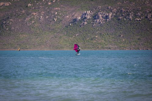 Free Windsurfers enjoying an adventure on pristine turquoise waters with scenic rocky hills in the background. Stock Photo