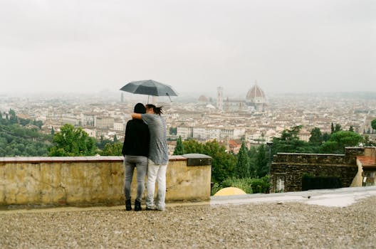 A couple embraces under an umbrella, enjoying a scenic view of Florence, Italy.