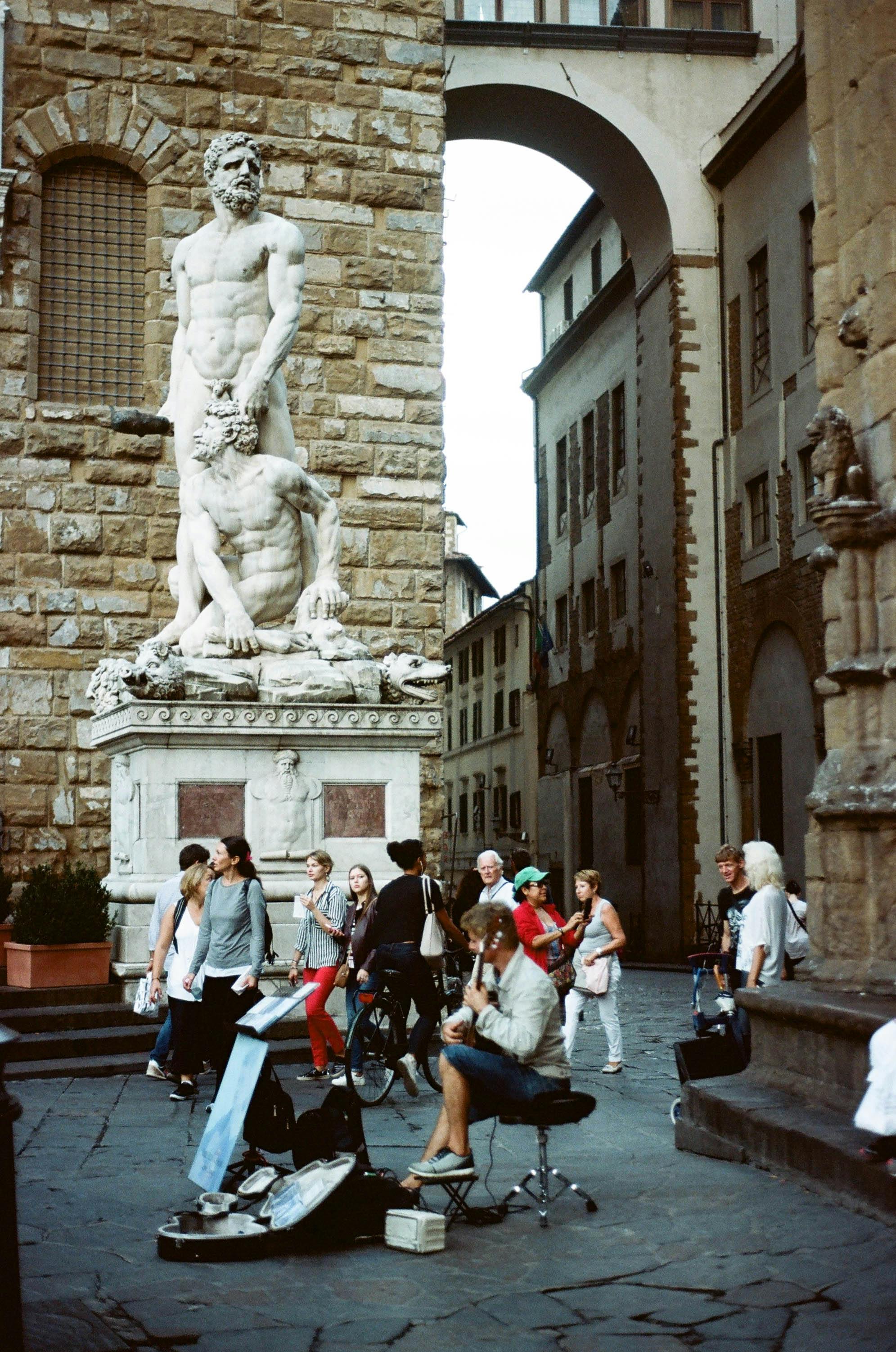 Street musicians performing near famous statue in Florence, capturing lively street atmosphere.
