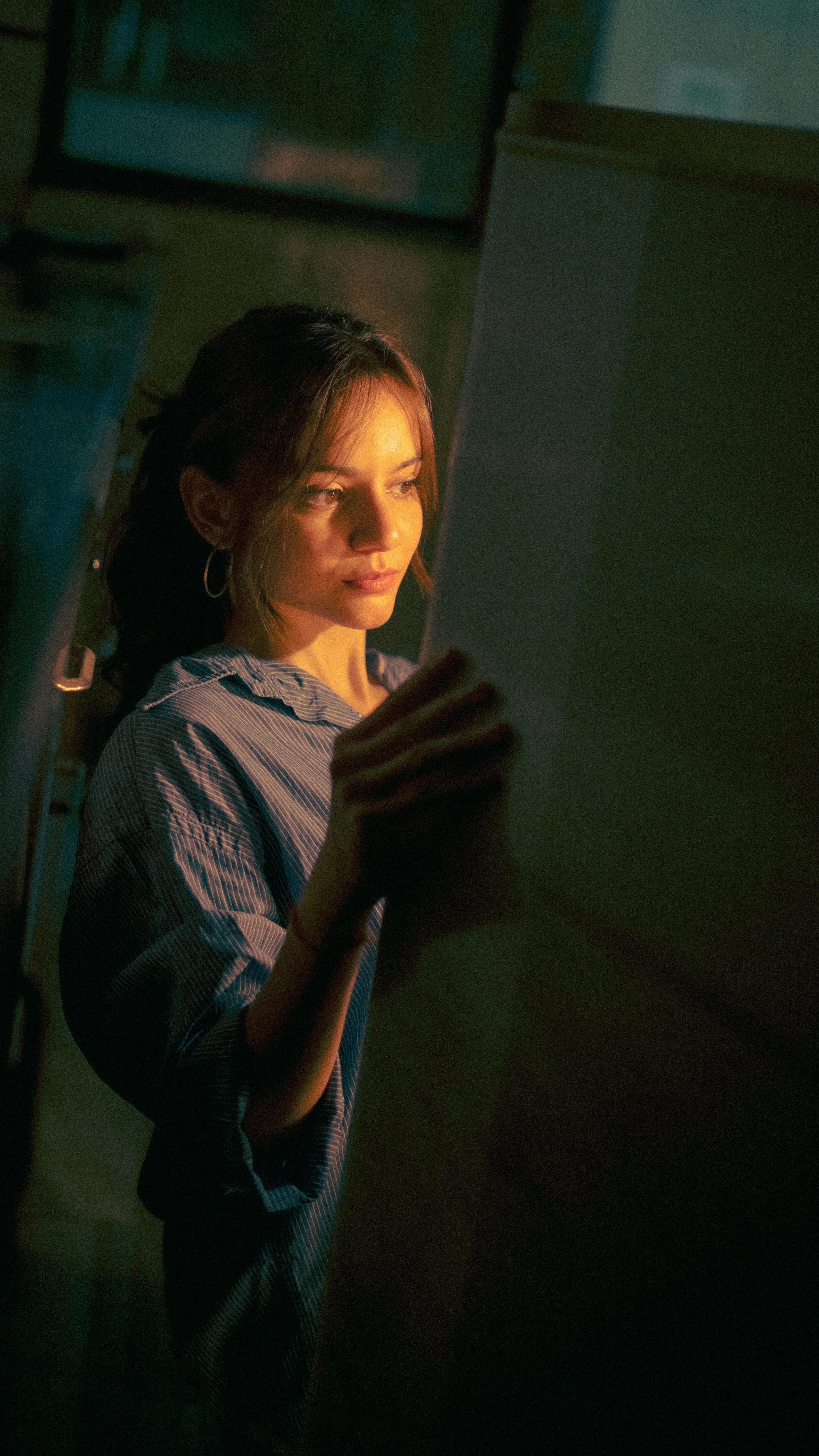 grátis Uma mulher em um espaço mal iluminado observando pensativamente uma grande obra de arte ou documento. Foto profissional