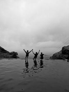 Three friends joyfully celebrating by a mountain pool at Ghatghar, India, in a captivating black and white setting.