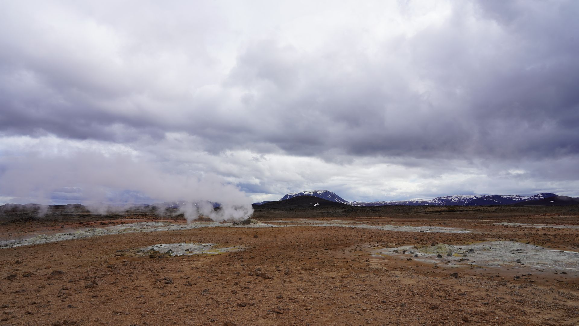 Geothermal steam rises in Iceland's rugged landscape under a dramatic cloudy sky.