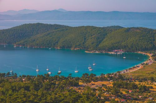 Free A beautiful coastal village with sailboats amidst lush green hills during sunset. Stock Photo