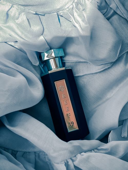 Free Luxurious perfume bottle resting on soft blue fabric, evoking elegance and sophistication. Stock Photo