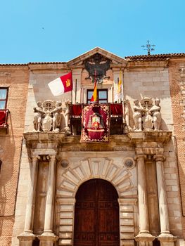 Ornate facade of a historic building adorned with statues and flags under a clear blue sky.