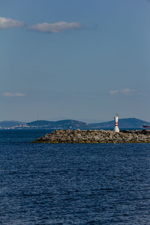 Free Peaceful seascape featuring a lighthouse on a rocky shore under clear skies. Stock Photo