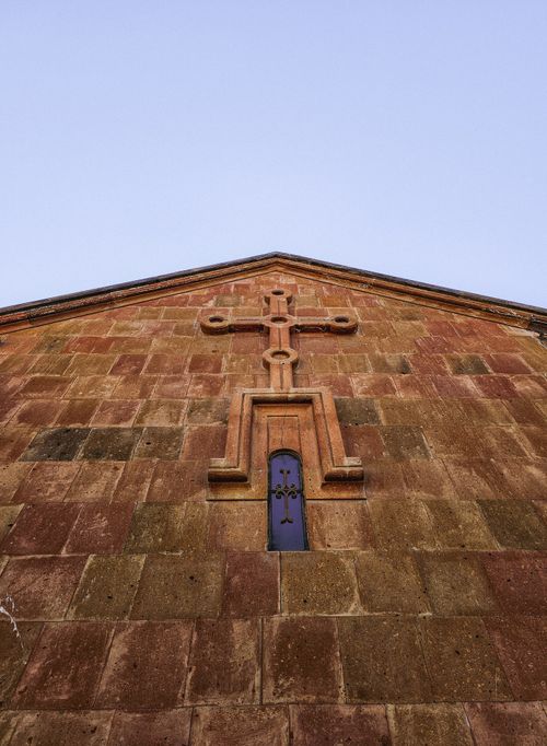 Free Close-up of a stone church facade featuring a prominent cross under a clear sky. Stock Photo