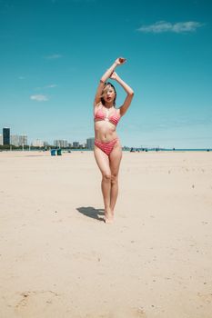 A woman in a striped bikini poses on Montrose Beach, Chicago, under clear blue skies.