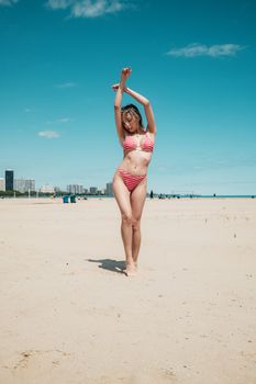 A woman in a pink bikini poses on a sunny day at Montrose Beach, Chicago, with city skyline in the background.