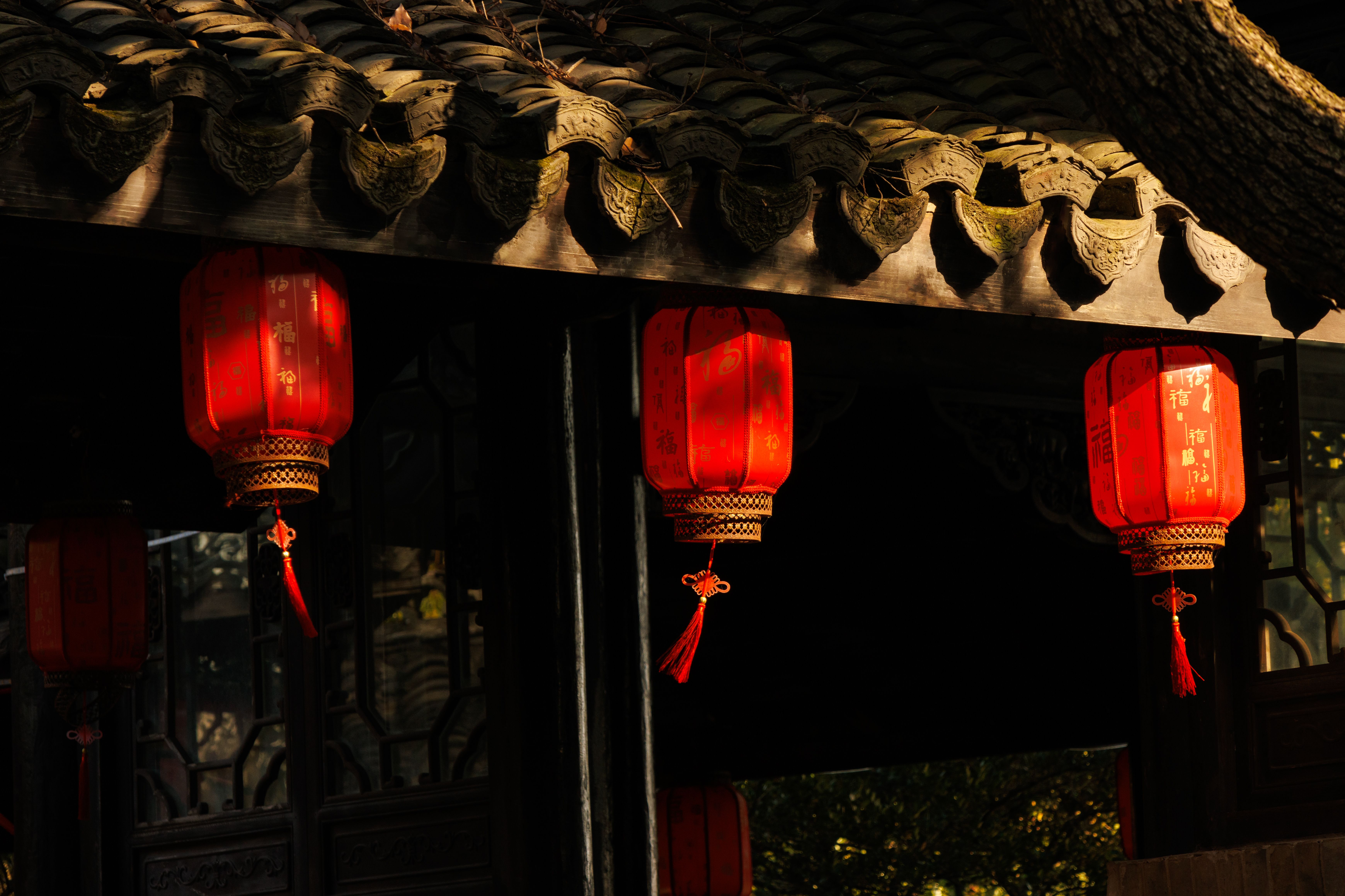 Red Chinese lanterns hanging on a traditional building facade in sunlight.