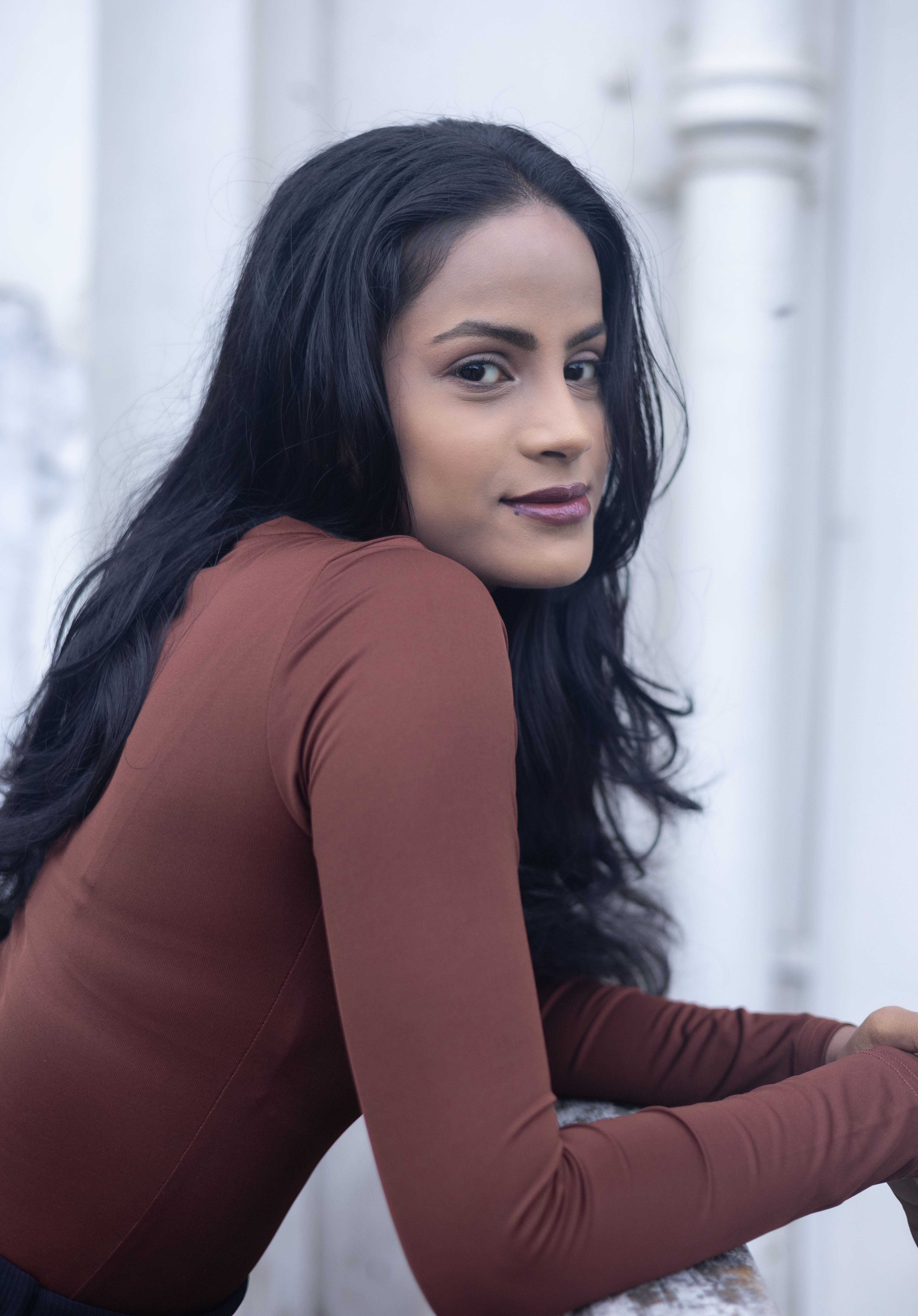 Elegant portrait of a woman leaning on a railing, featuring long black hair and a confident expression.