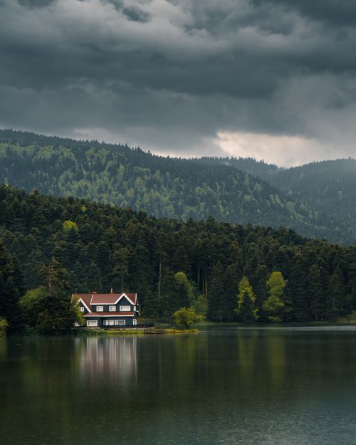 Free A serene lake house surrounded by lush forests in Gölcük Köy, Bolu, Türkiye under a dramatic cloudy sky. Stock Photo