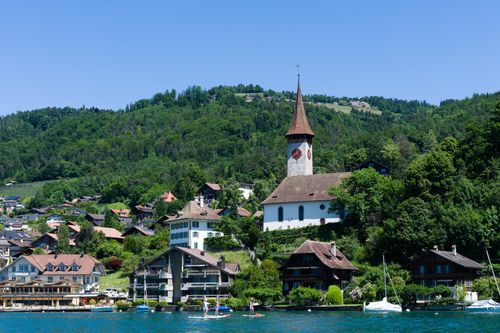 Free Charming village on Lake Thun with iconic church and lush hills in Switzerland. Stock Photo