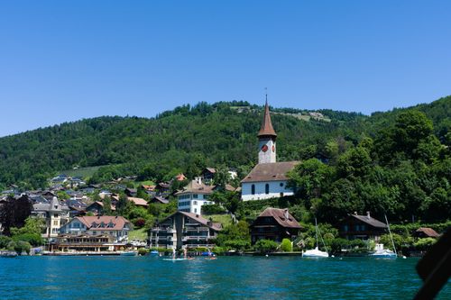 Free A picturesque view of Spiez, Switzerland with the iconic church and Lake Thun under a clear blue sky. Stock Photo