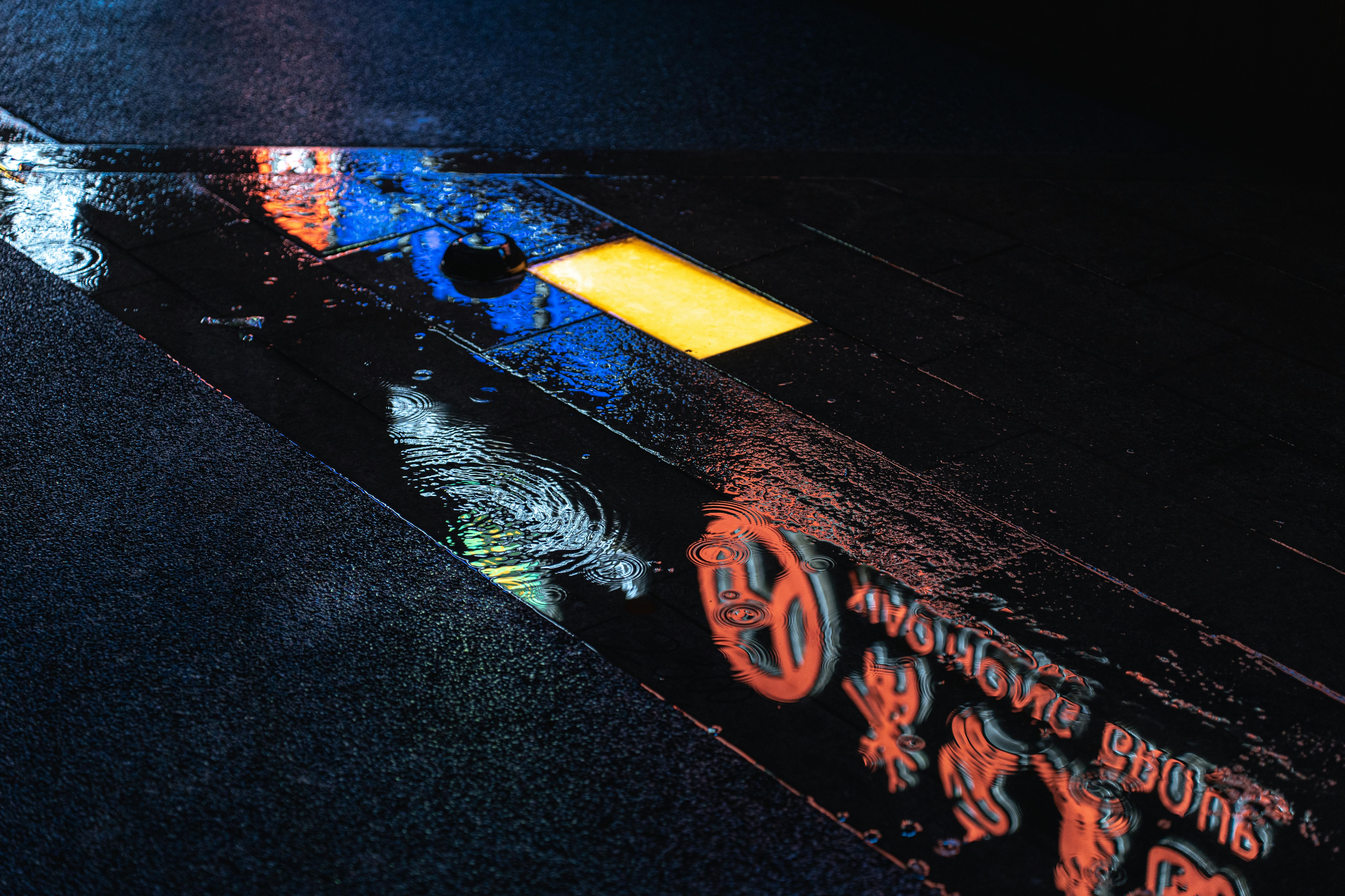 Vibrant neon signs reflect on the wet pavement at night, creating a colorful urban scene.