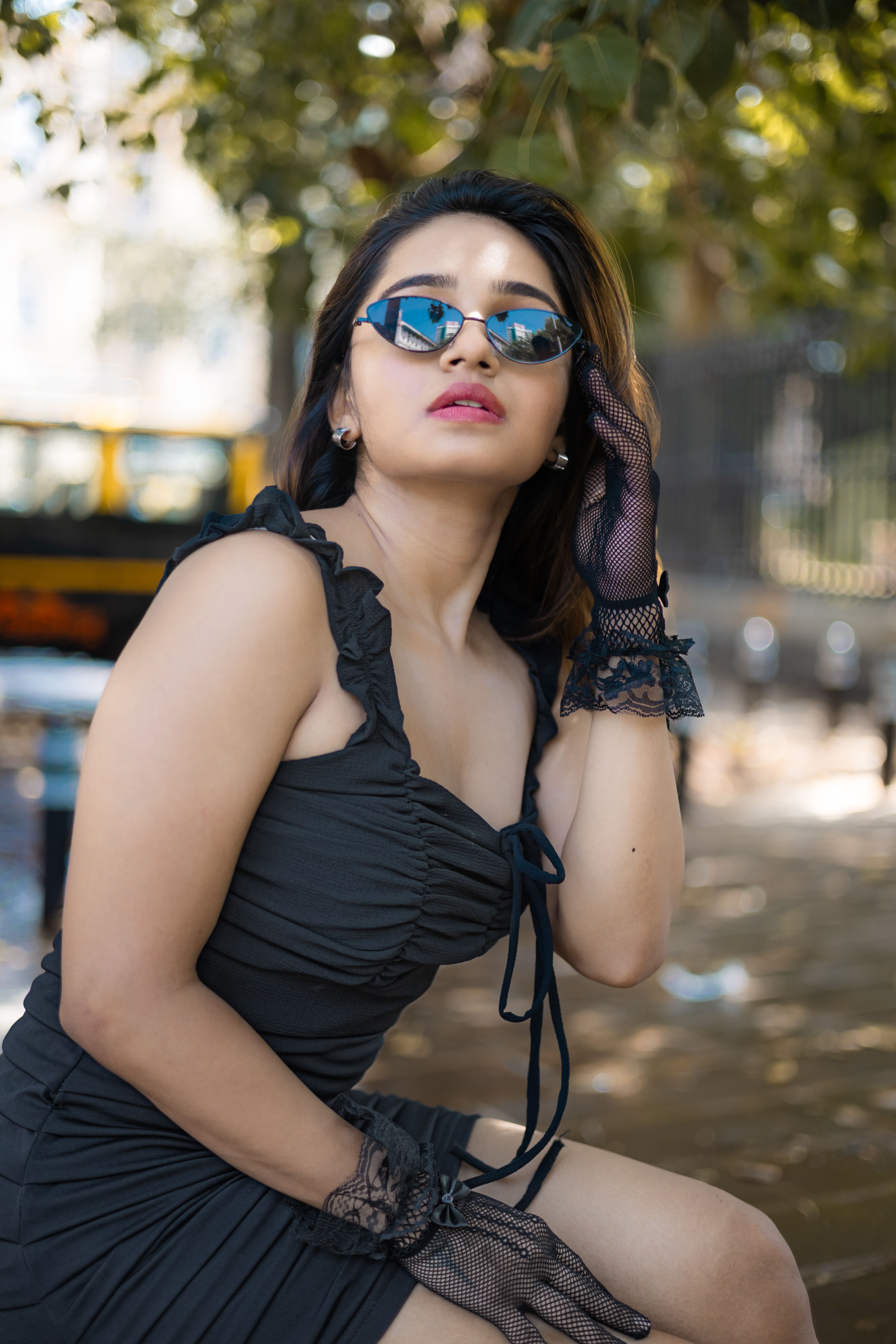 Stylish woman in black dress and sunglasses posing confidently outdoors.