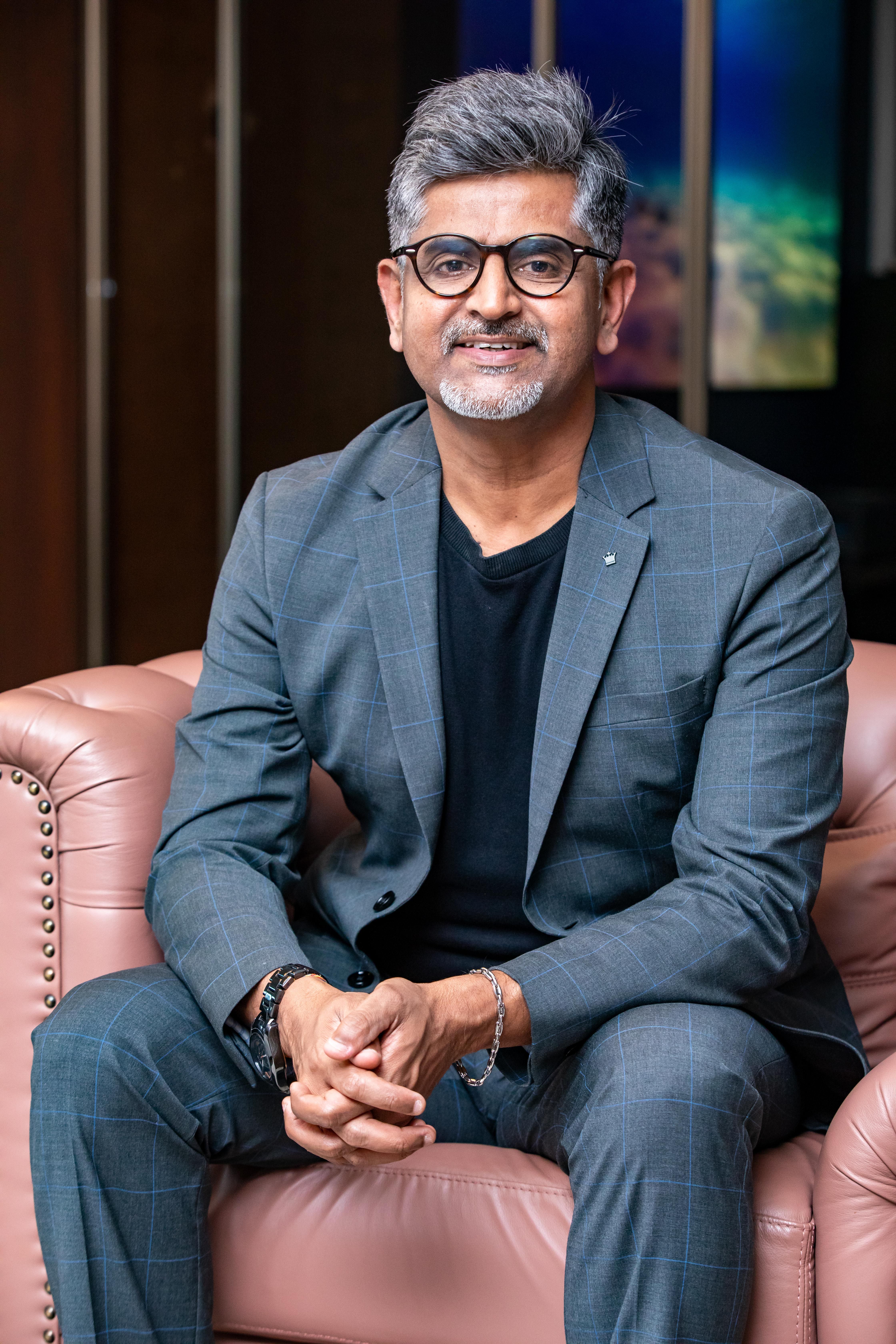 A man in a stylish business suit sits confidently on a leather couch indoors.