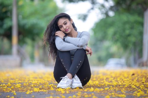 Free Portrait of a relaxed young woman sitting on a yellow leaf-strewn path in a park setting. Stock Photo