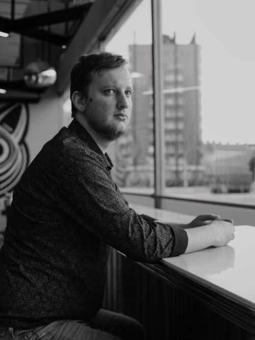Free Candid black and white portrait of an adult male sitting by a window in an urban setting indoors. Stock Photo