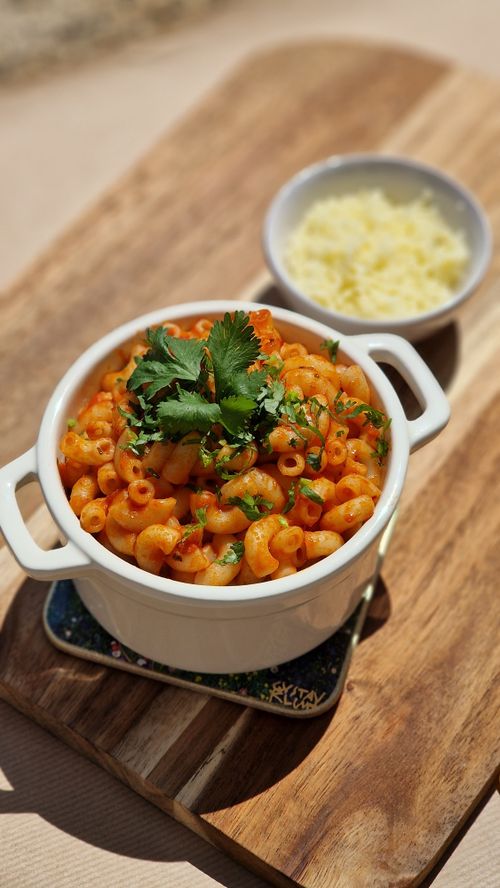 Free A mouth-watering bowl of macaroni pasta garnished with fresh cilantro and accompanied by grated cheese. Stock Photo