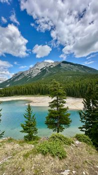 Majestic mountain view with clear lake and lush forest under a bright blue sky.