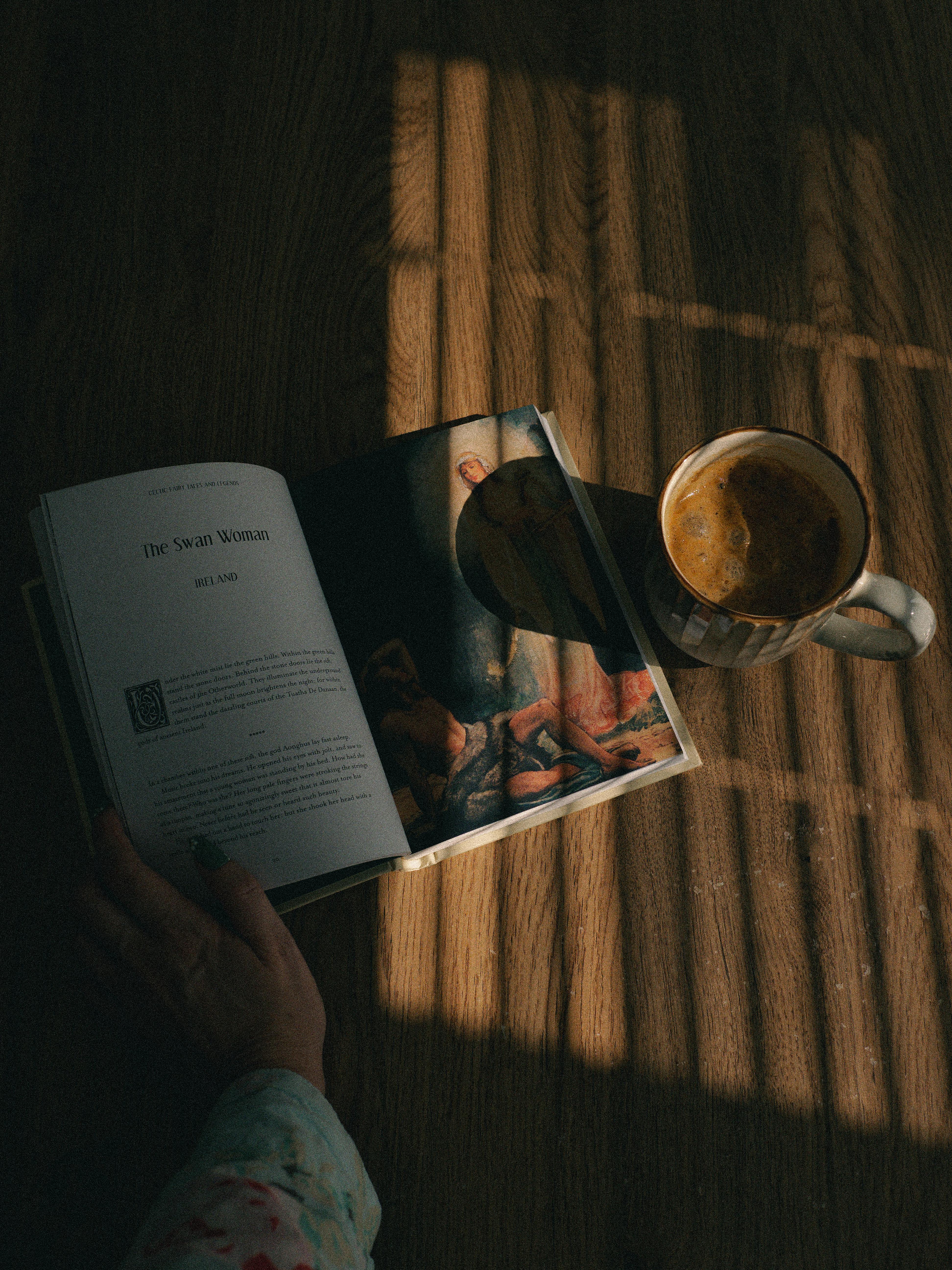 Gratis Una escena tranquila de un libro y un café sobre una mesa de madera iluminada por el sol, que invita a la relajación. Foto de stock