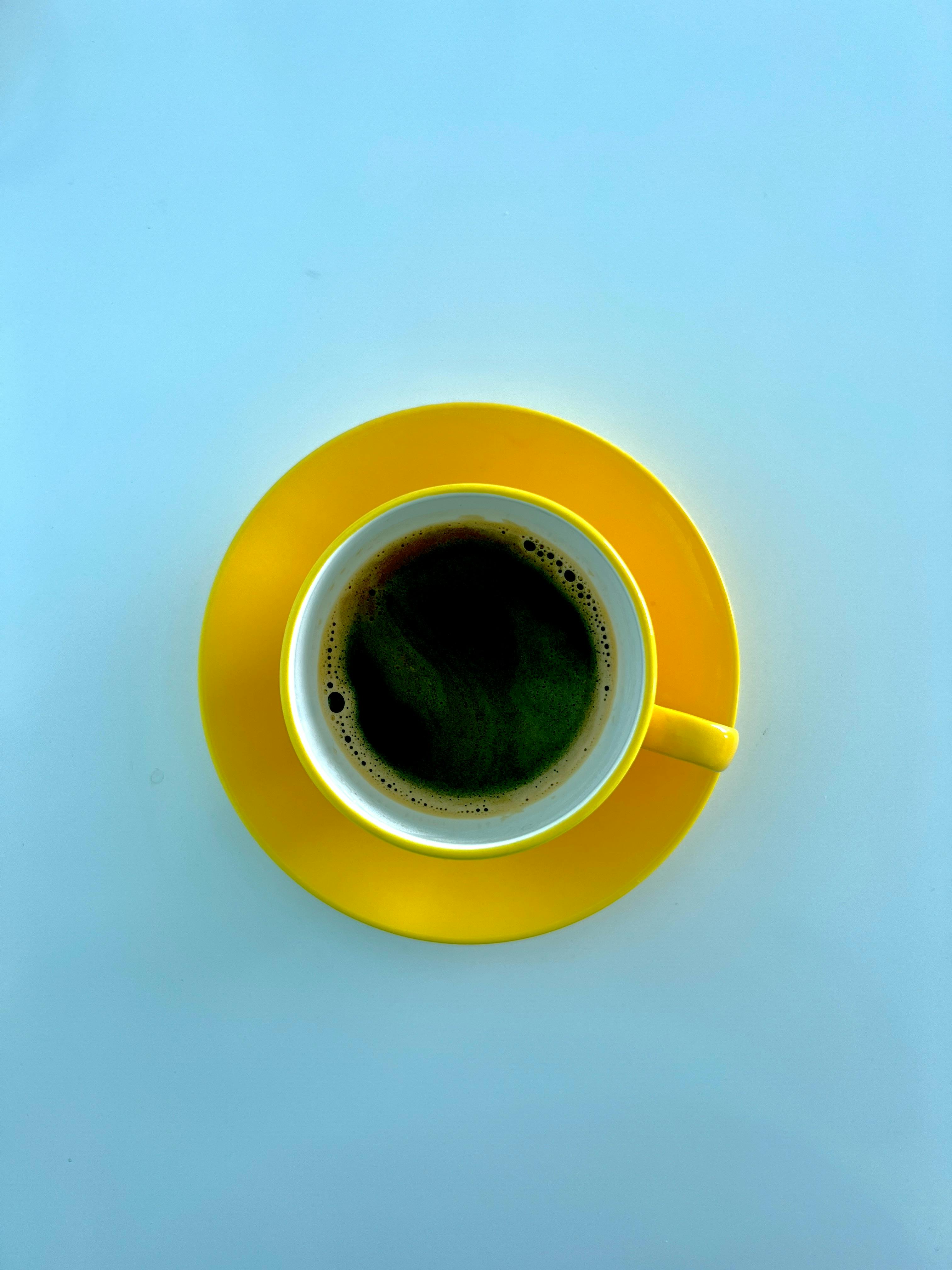 Gratis En kaffekopp på en fargerik gul tallerken mot en ren bakgrunn sett ovenfra og ned. Arkivbilde