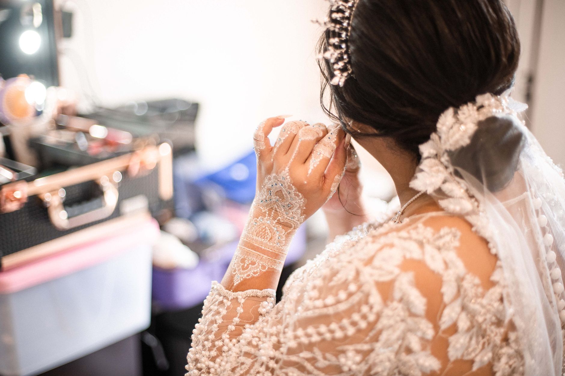A bride in an elegant lace gown applies makeup, getting ready for her wedding.