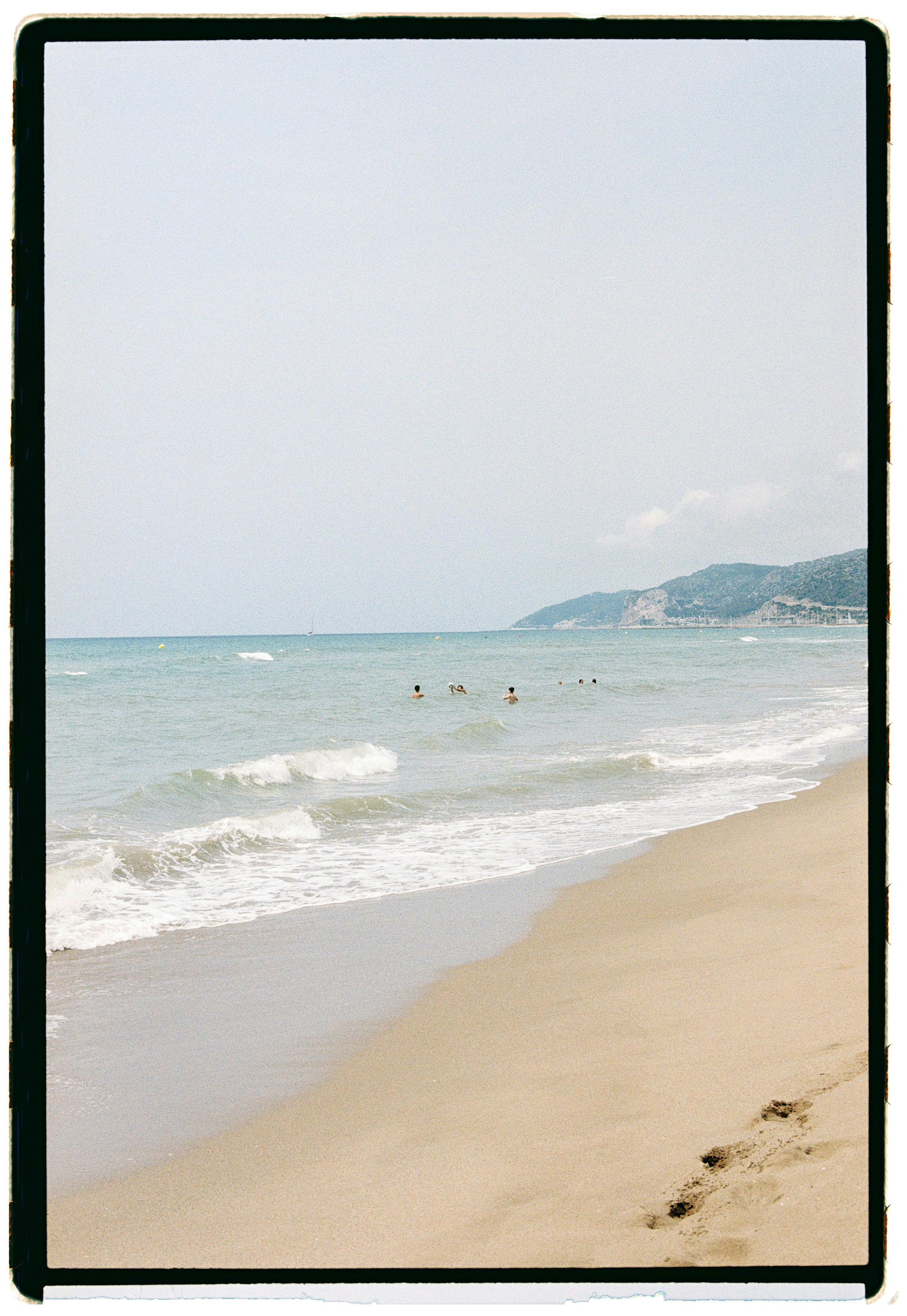 Peaceful sandy beach with gentle waves and distant swimmers in summer.
