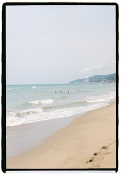 Peaceful sandy beach with gentle waves and distant swimmers in summer.