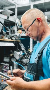 Skilled technician with gray hair working attentively in a cluttered workshop environment.