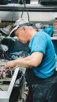 Skilled technician working on electronic equipment with precision tools in a busy workshop.