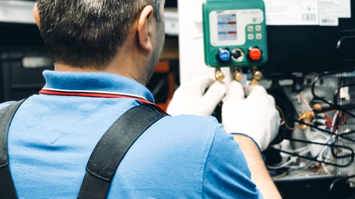Técnico de luvas usando um manômetro para conferir a tubulação de um ar-condicionado